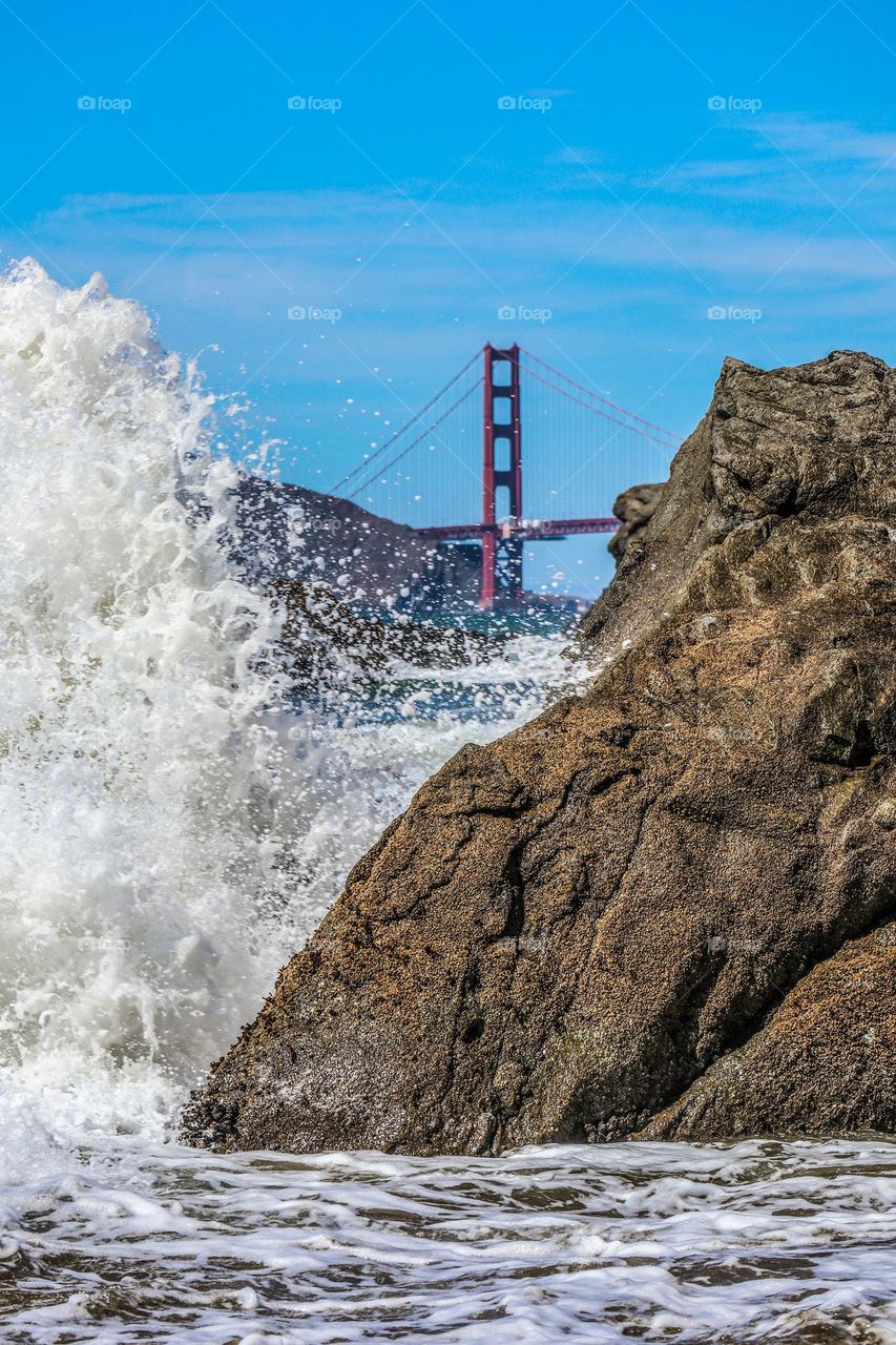 View from lands end beach in San Francisco California with the waves crashing up against the rocks with the Golden Gate Bridge in the background on a warm afternoon