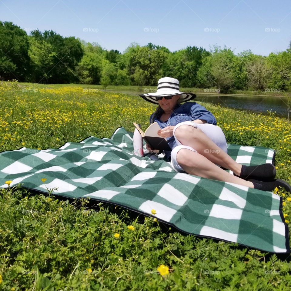 A woman in a field of flowers reading a book on a blanket enjoying the Countryside