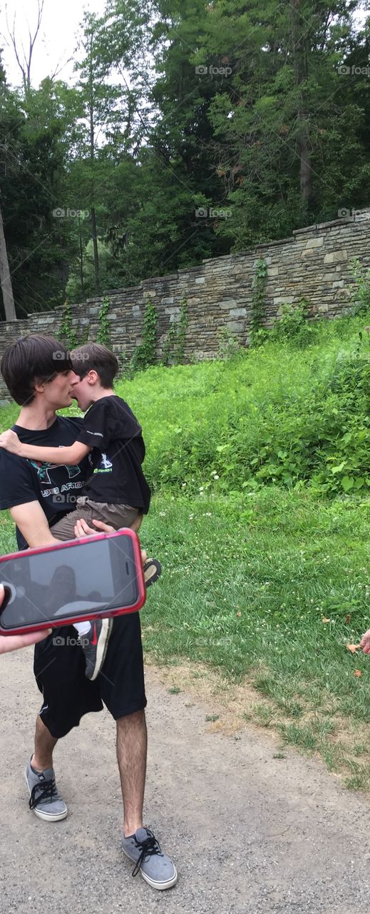 Fifteen year old boy carrying his younger brother and trying to console him on a walk in the country park.