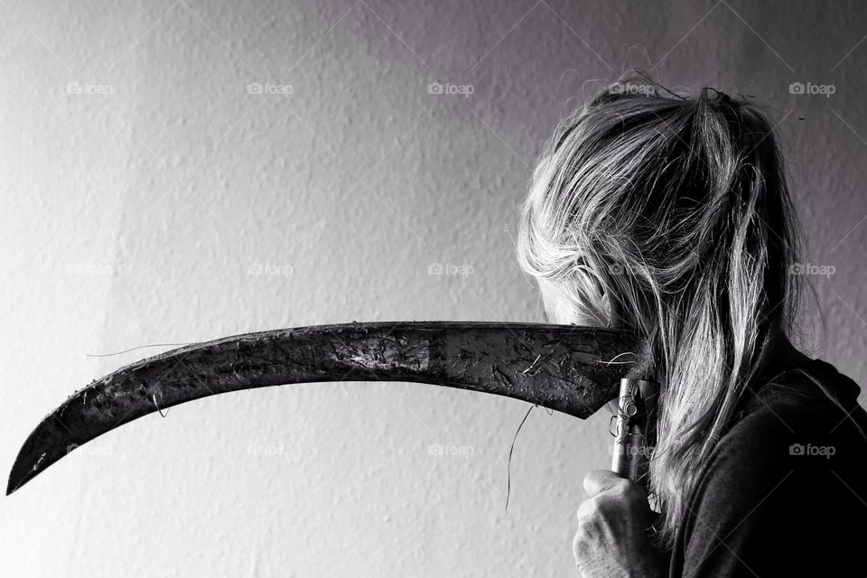 Black and white photo of a woman with a ponytail leaning on a scythe with grass after work 