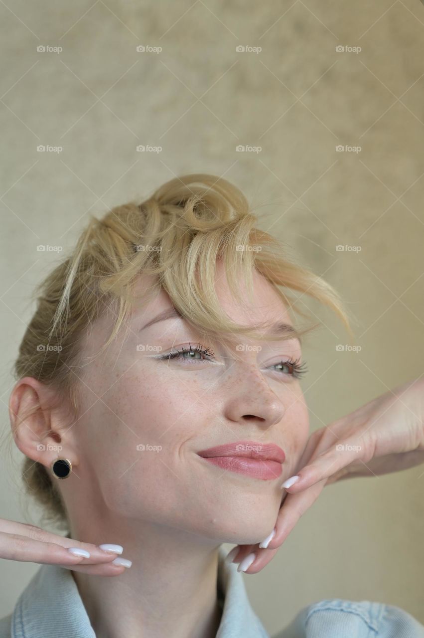 Portrait of a cute girl with blond hair with a beautiful look with her hands near her head