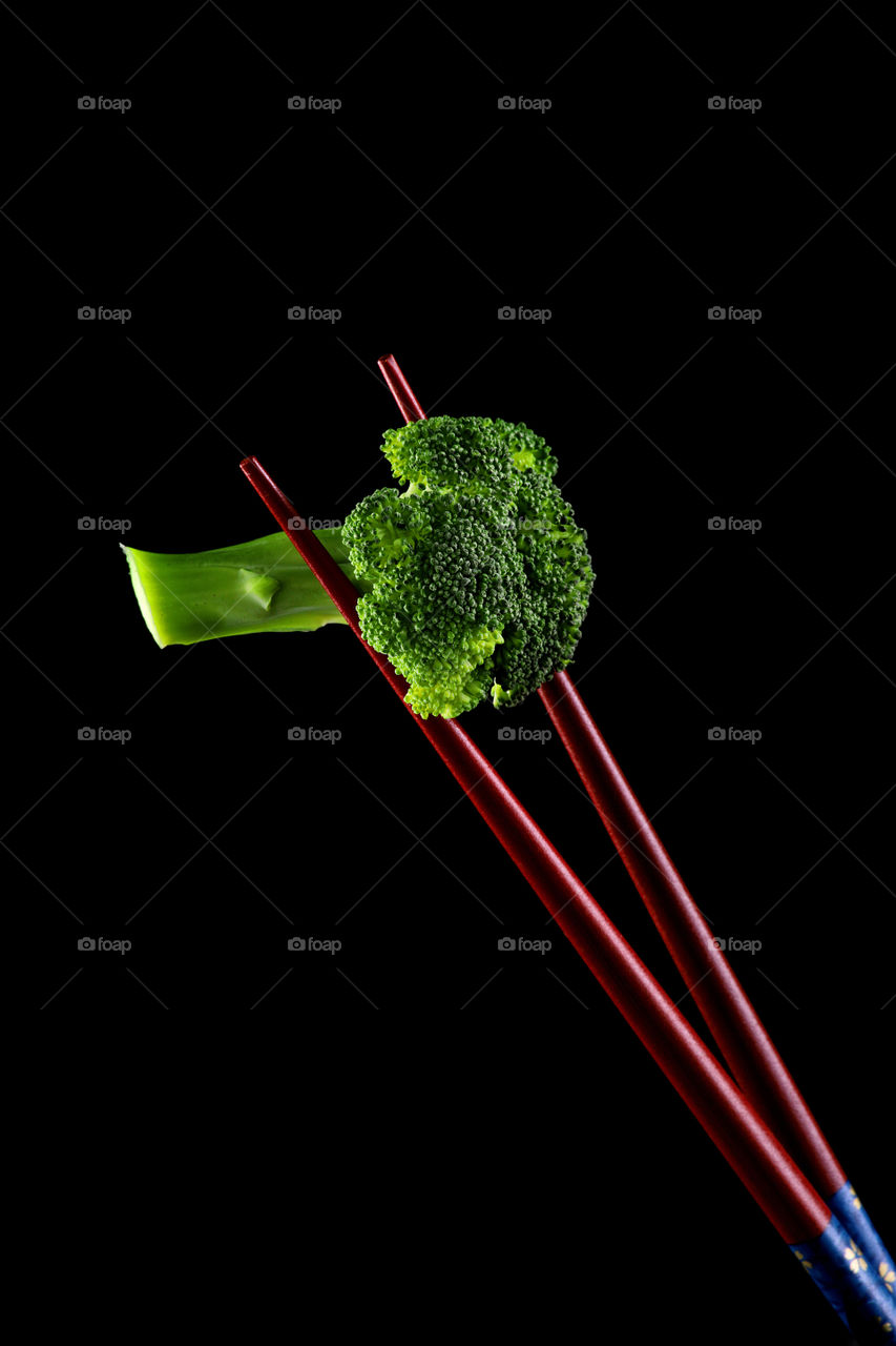 fresh green broccoli with chopsticks on black background