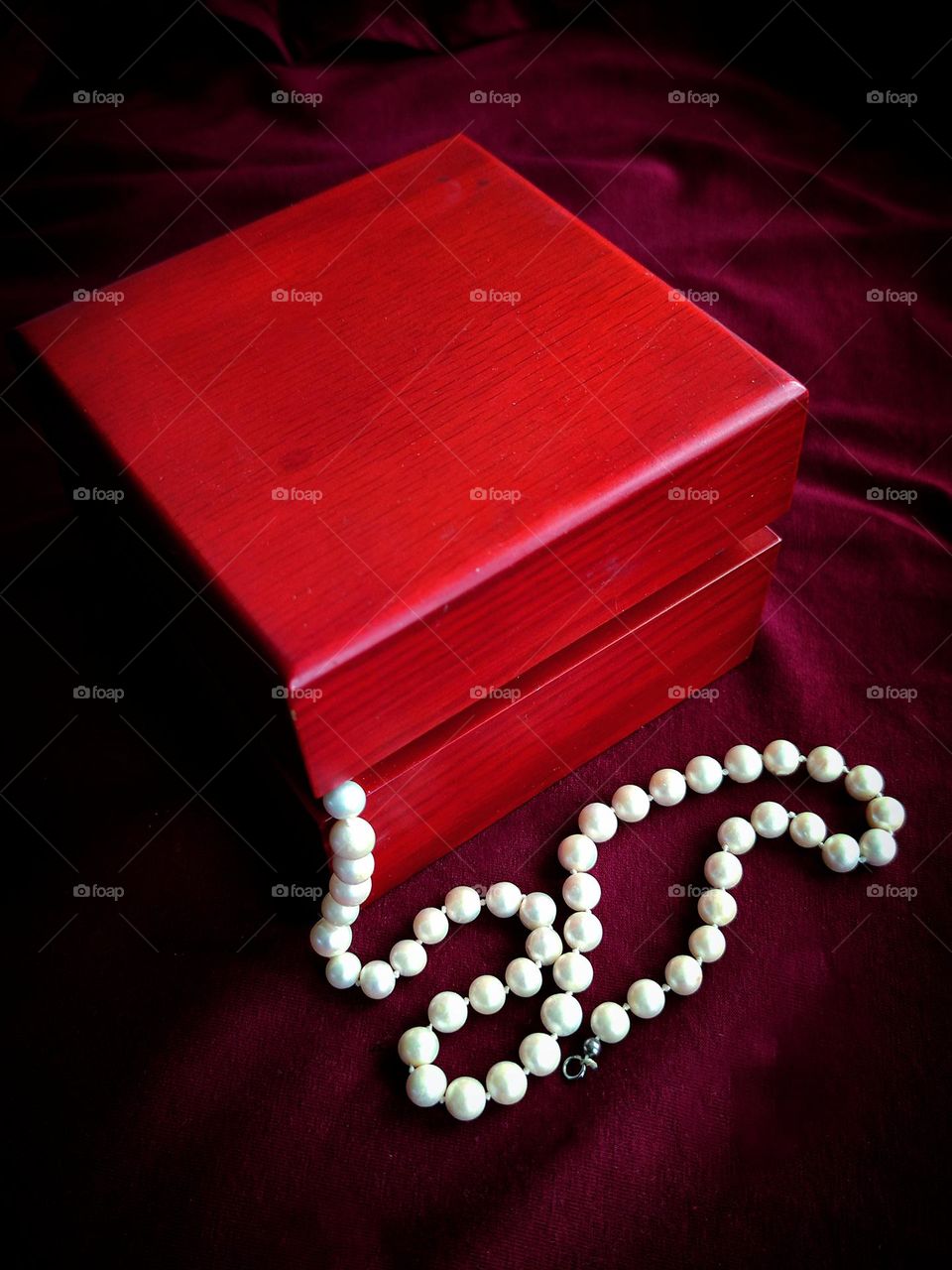 On a purple-red background is a wooden red box.  Hanging from the box is a white pearl thread that contrasts with the background.