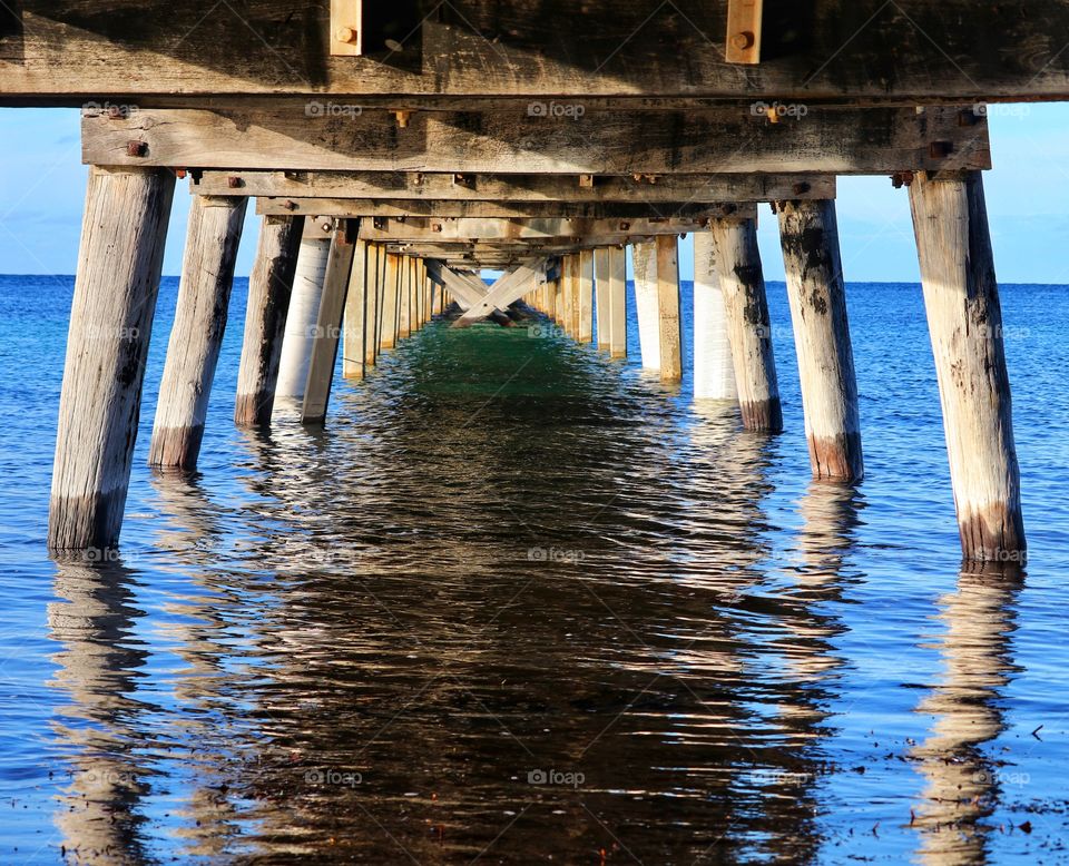 Perspective and reflection View underneath a weathered wood public fishing dock, Jetty, pier, wharf, south Australia, vibrant ocean colours on sunny day