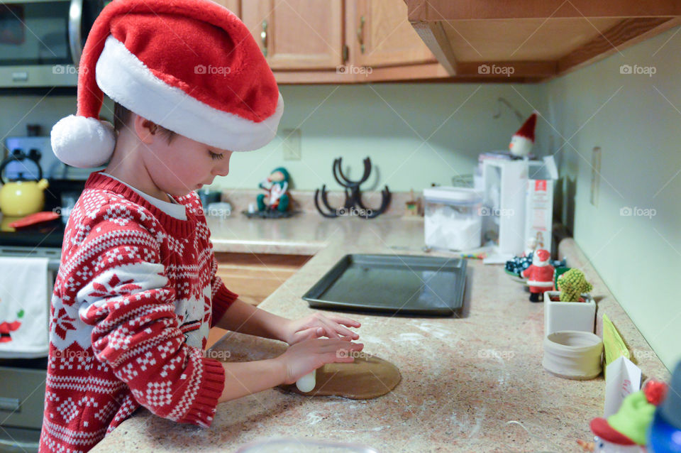 Young boy wearing a Santa hat while rolling cookie dough for Christmas cookies in a kitchen