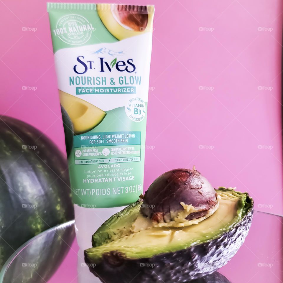 St. Ives avocado face moisturizer accented by a fresh avocado half with a contrasting pink background.