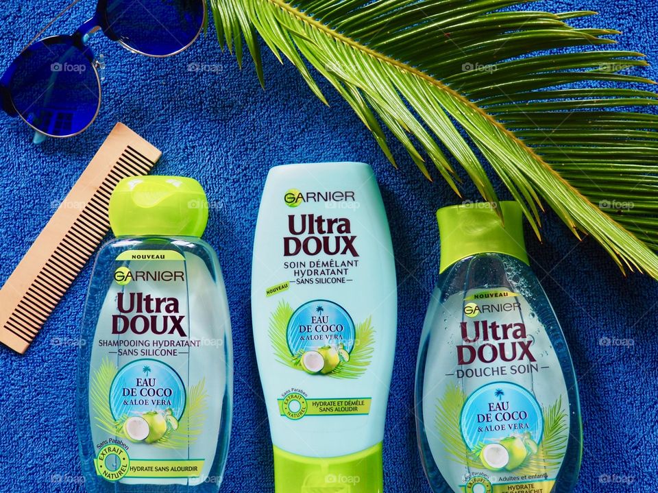 Garnier shampoo, conditioner and bath gel on a blue towel with comb and palm leaf and blue sunglasses.