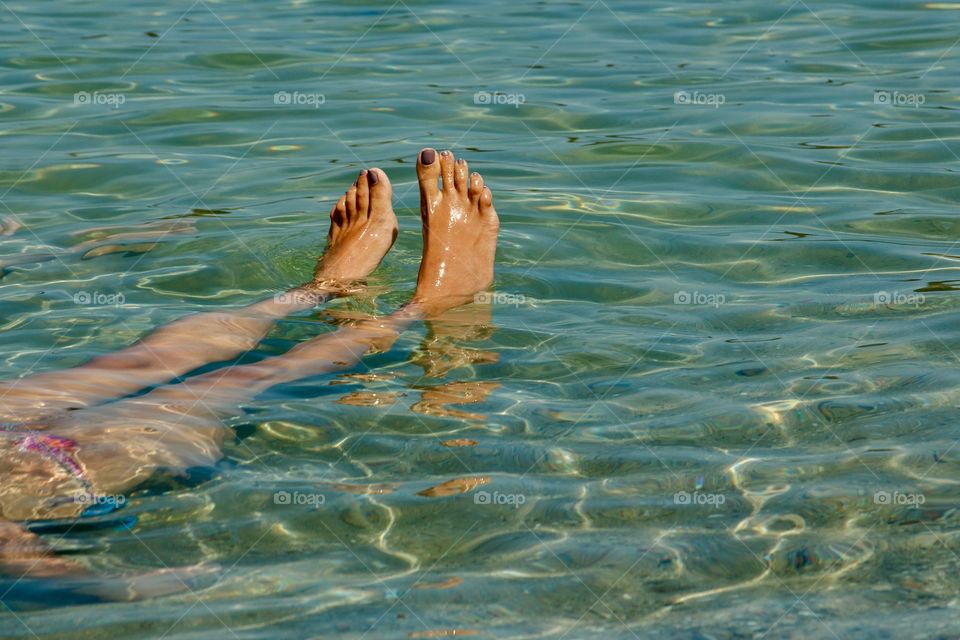 Woman’s feet in crystal clear water of Mediterranean Sea. Summertime