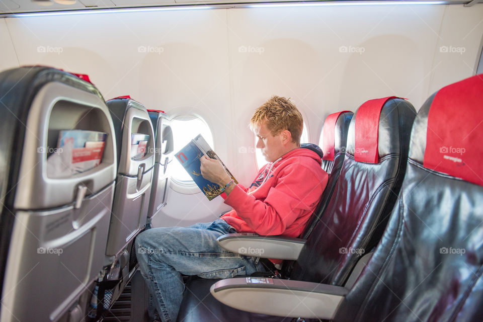 Male passager reading the tax free catalig in a airplane.