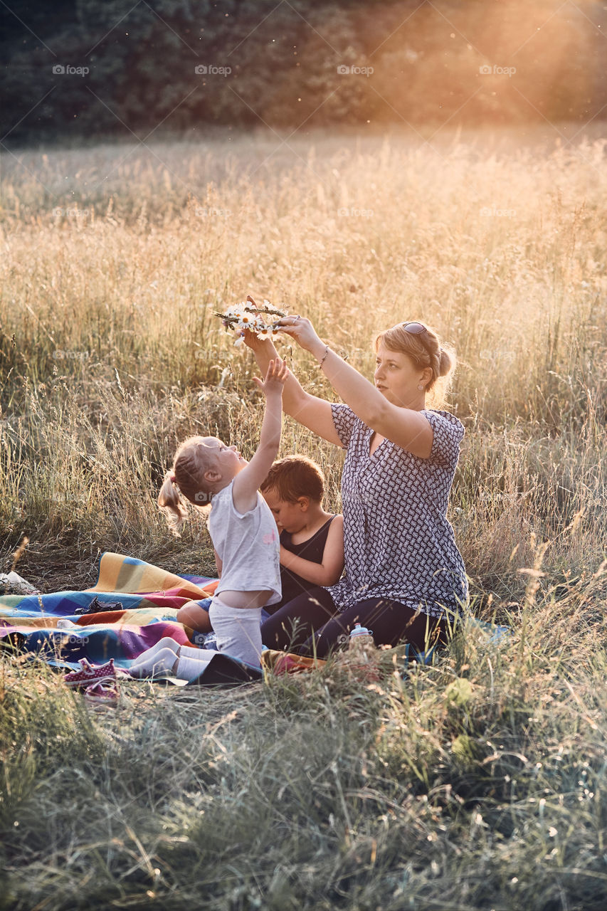 Family spending time together on a meadow, close to nature, parents and children playing together, making coronet of wild flowers. Candid people, real moments, authentic situations