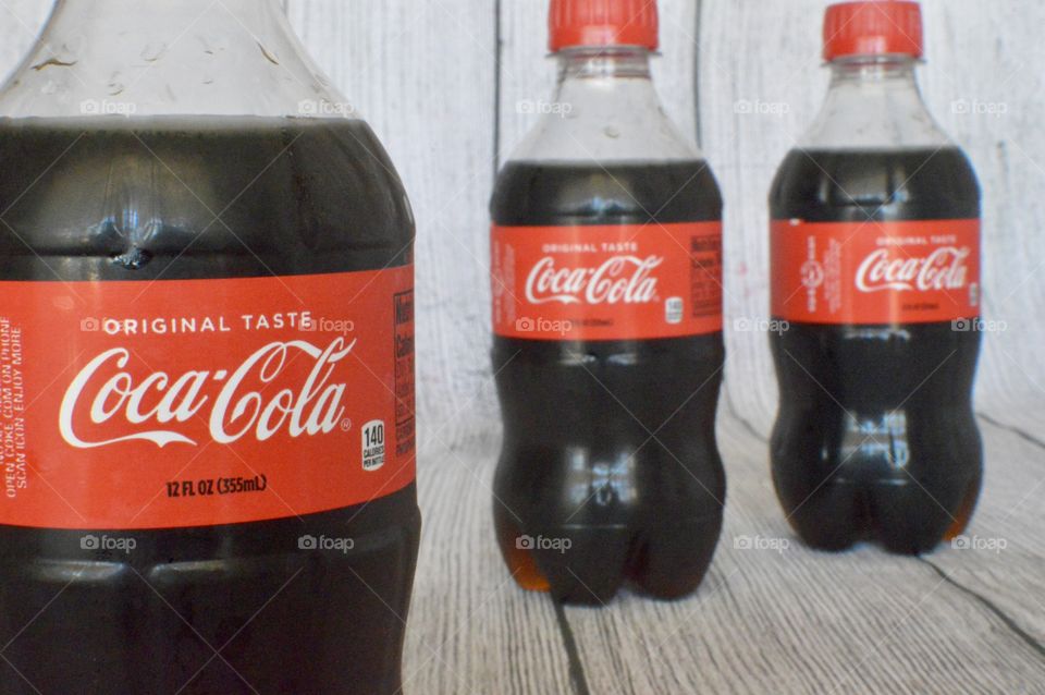 Three plastic bottles of Coca-Cola on a white rustic background