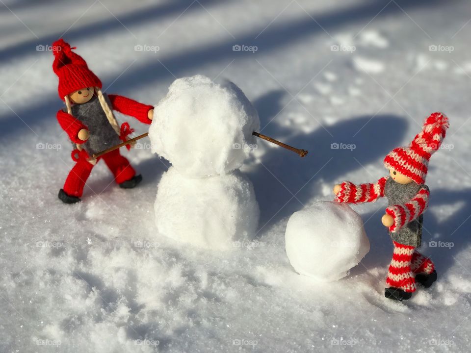 two wooden dolls girl and boy build a snowman from snow, winter sunny day
