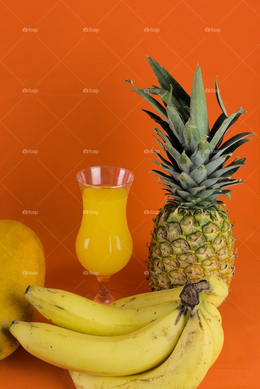 Natural fruit next to a glass with natural juice and orange background