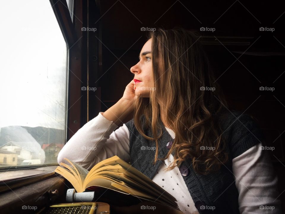 Woman in train sitting next to the window and looking outside with a book in her hand