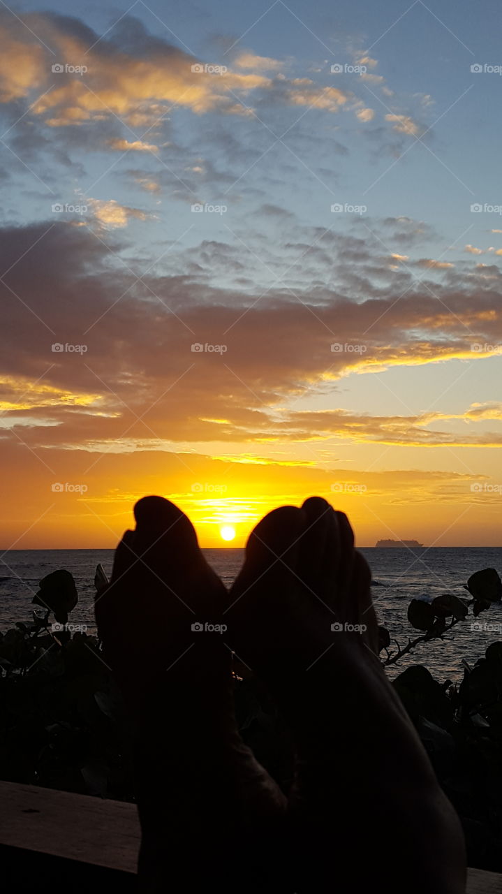 bare feet frame tropical sun set as cruise ship sails into distance