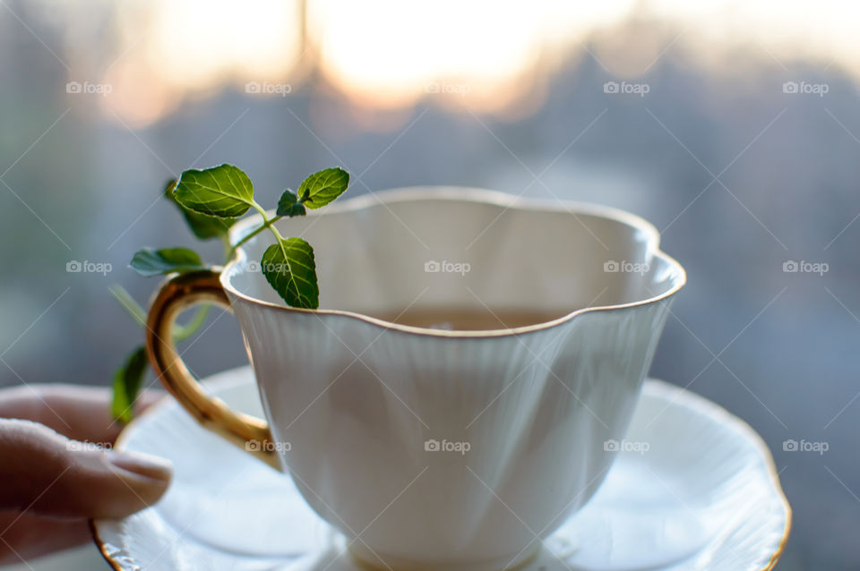 Hand holding cup of tea with mint leaf