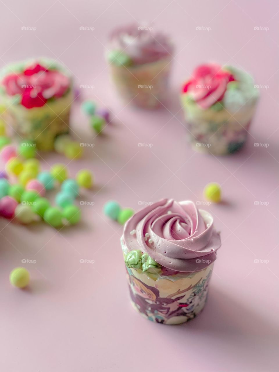 Purple and pink cupcakes on a pink table top with colourful sweets and candies 