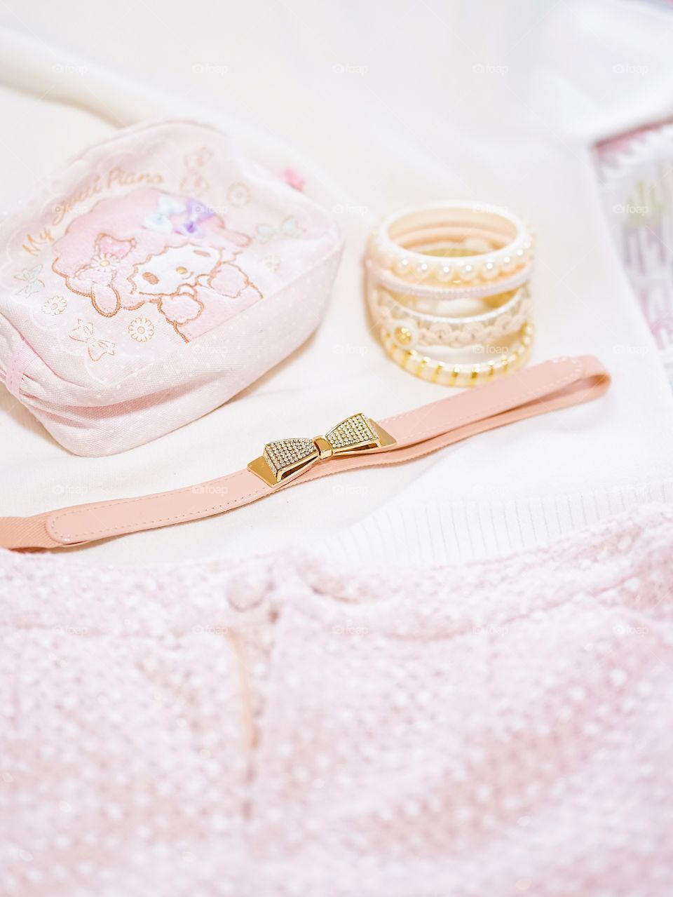 Lady's accessories. Pink theme of lady belongings including sweater, cosmetic bag, shorts, cute belt and bracelets. Selective focus on the bow belt. Lady traveling and fashionista concept.