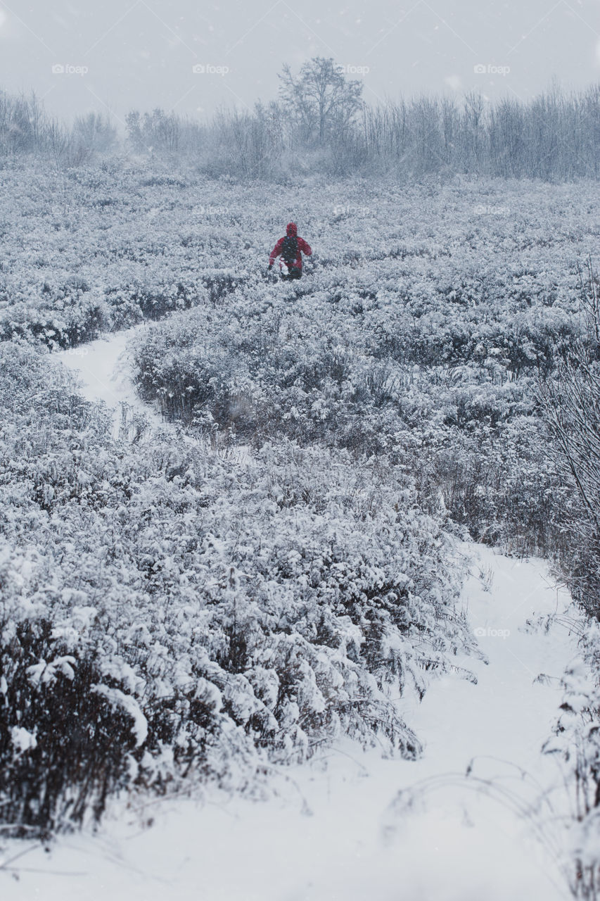 Young man jogging through meadow pathway during heavy snowing. Workout outdoors during winter snow storm