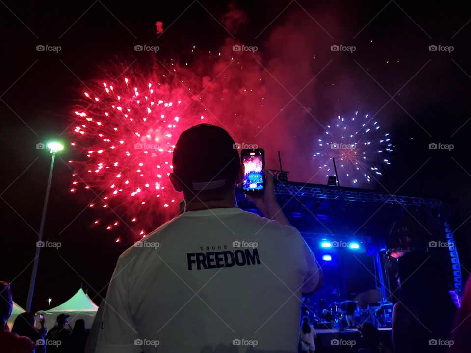 A July 4th fireworks and concert celebration with a man wearing a T shirt for a July 4th 2023 opening movie called The Sound of Freedom. A movie about a true story of an American hero saving trafficked children.