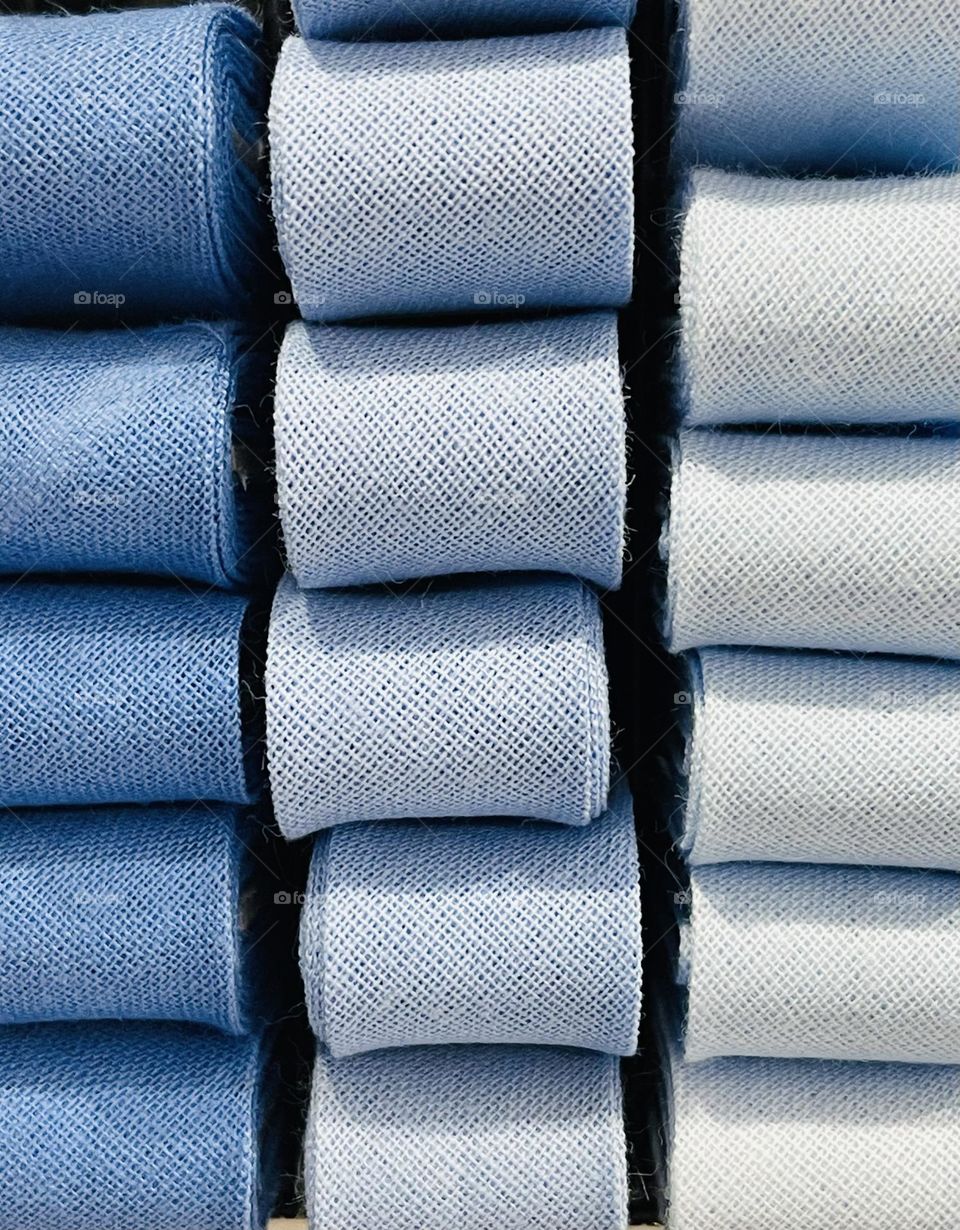 cotton ribbons of various shades of blue folded and lined up on display on the shelf of a haberdashery