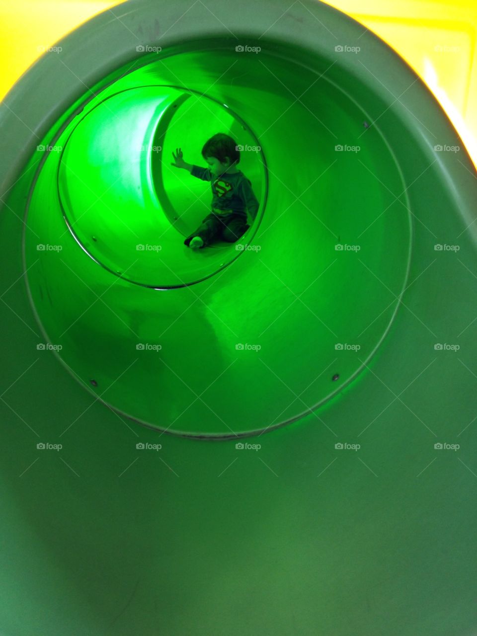 Child playing in a green tunnel in a play structure. 