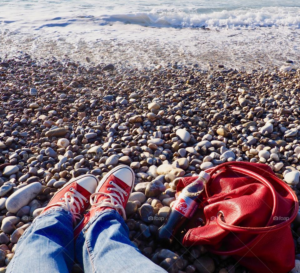 A bottle of Diet Coke on the beach with red sneakers and red leather bag.