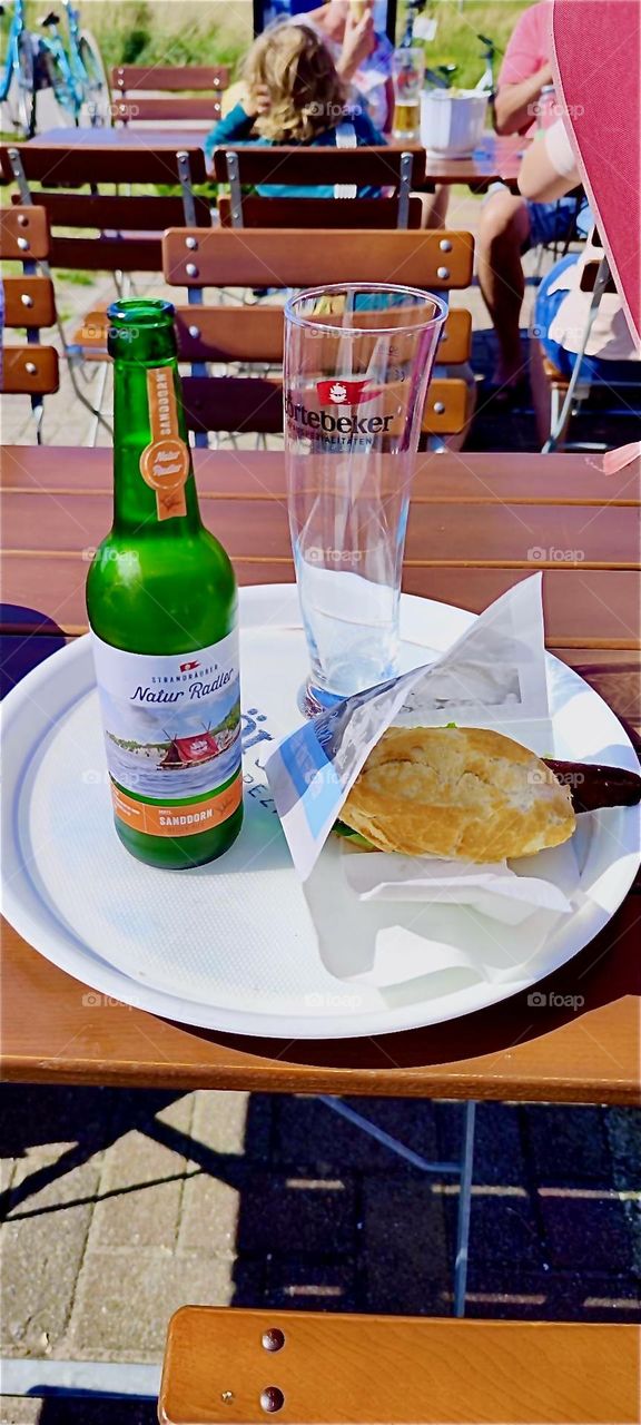 Lunch on the beach of the island “Hiddensee” in the “Baltic Sea” in “Mecklenburg - Western Pomerania”, Germany is exquisite: a mackerel sandwich and a “Sanddorn Radler”, a mix of specialty beer and lemonade to wash it down. 2024. Hypnotic Productions