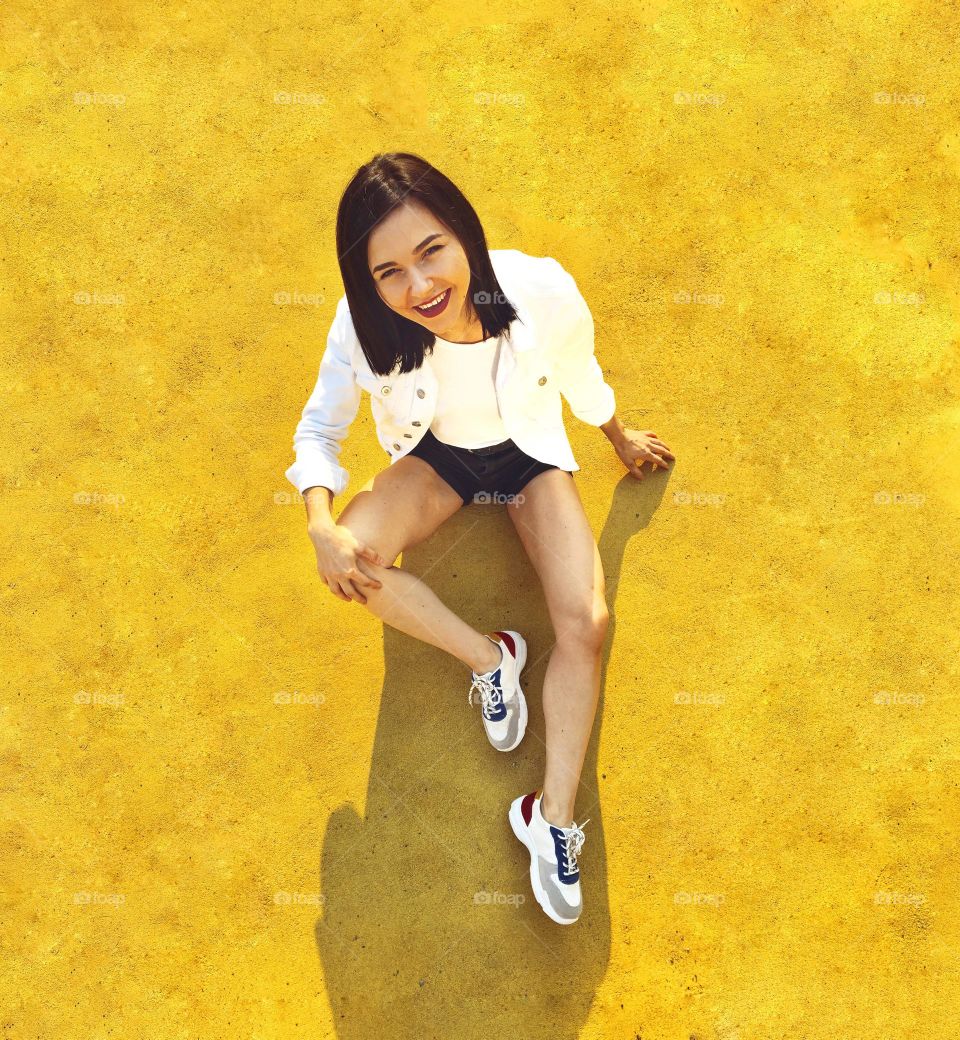 The girl sits on a yellow floor and smiles at the camera.