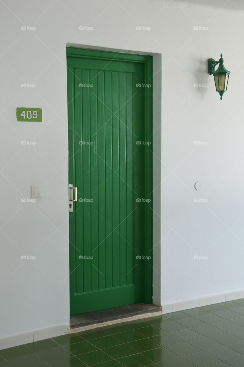 Photo of a green door, lamp and a white building wall