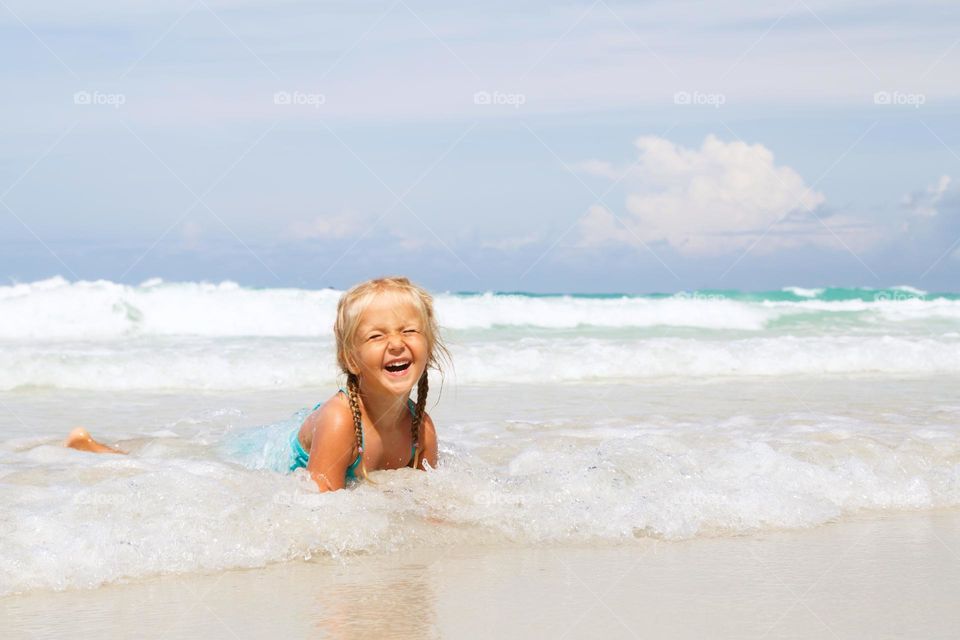 Happy little Caucasian girl with blonde hair having fun on sea at hot summer day 