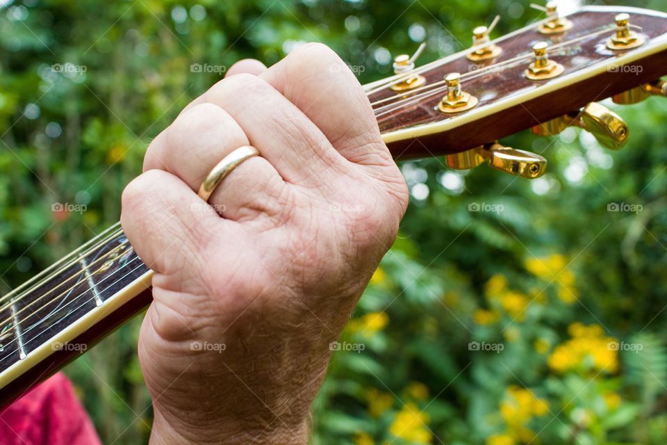 Close-up shot of an aging musician's hand on the neck of his guitar.