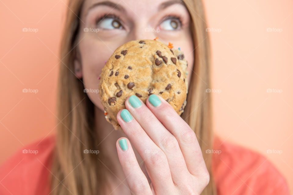 Woman playfully holding a chocolate chip cookie sandwich in front of her face 