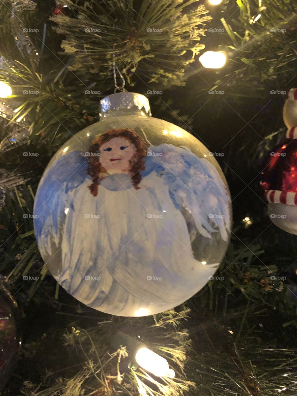 A  closeup of a glass ornament with an angel painted on it hanging on the tree. 