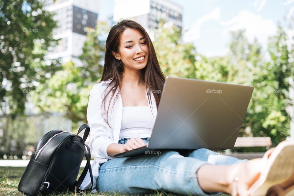 Young asian woman student freelancer with long hair working on laptop in city park