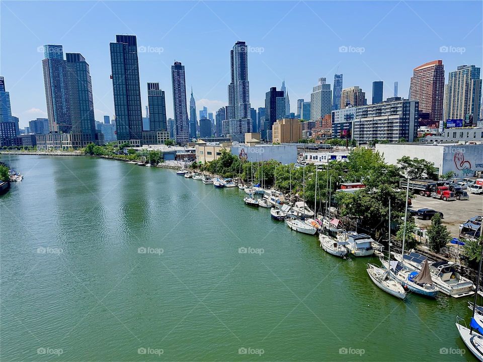A breathtaking panorama unfolds overlooking “Newtown Creek” with its numerous boats from the “Pulaski Bridge” that connects “Greenpoint”, Bklyn to LIC, Queens. In the distance we see “Manhattan” and the “Empire State Bldg”. 2024. Hypnotic Productions