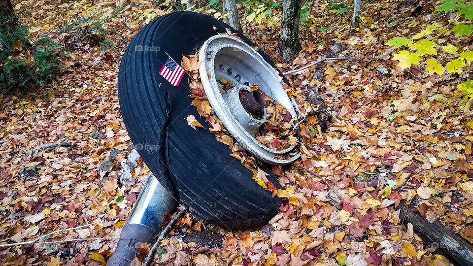 old aircraft tire abandoned in the autumn leaves with an American flag left In memorial.