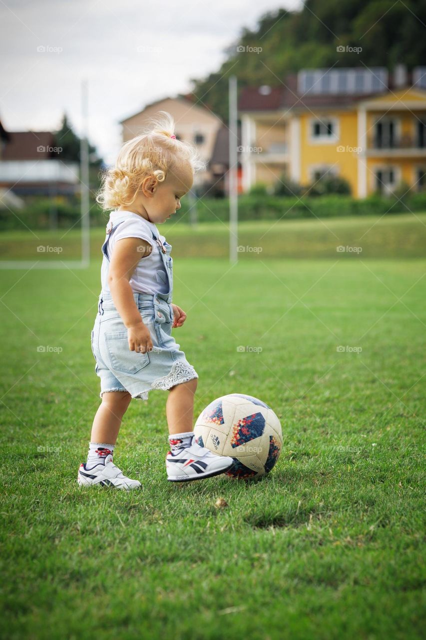 A little curly-haired girl kicks a soccer ball.