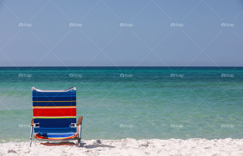 A beach chair on sugar white Florida beach with emerald colored ocean in the background