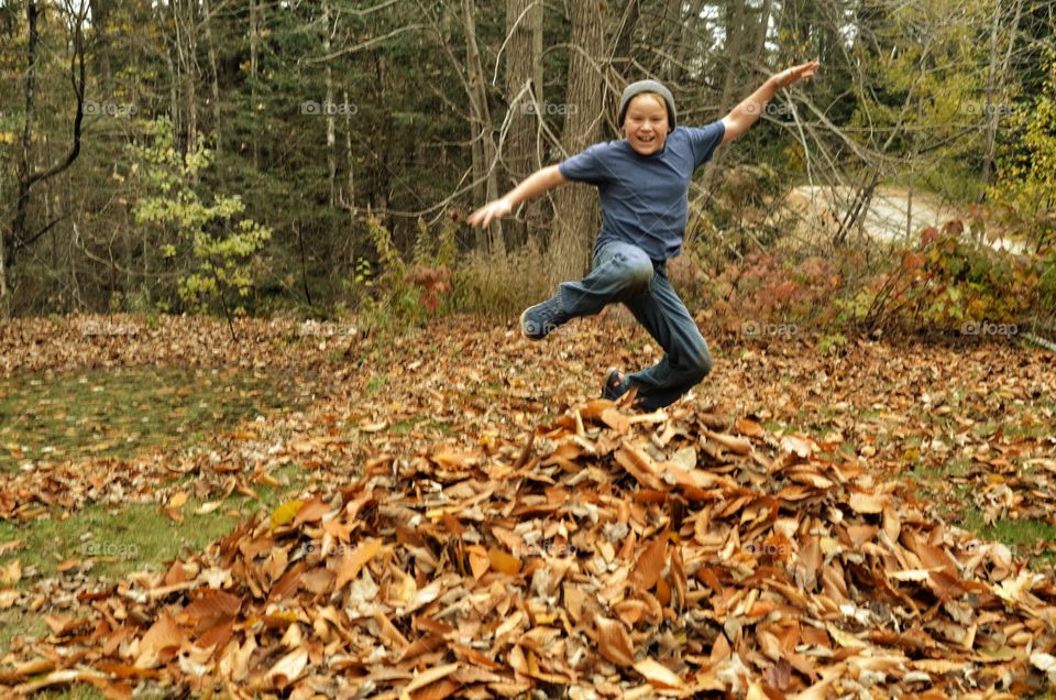 A boy jumping over autumn leaves