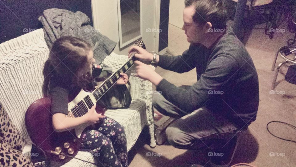 Cute little girl and her handsome father are playing guitar