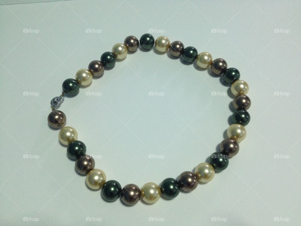 Black, brown, gold and white pearl necklace on white background.
