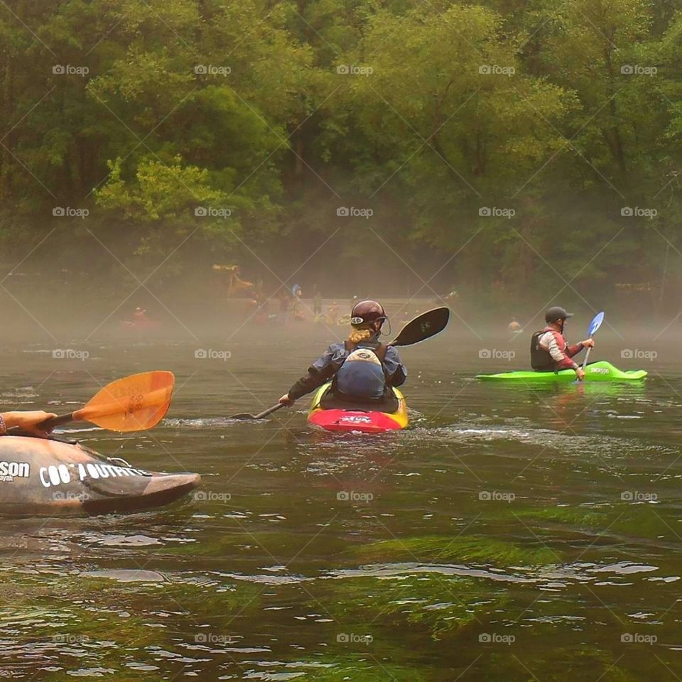 Colorful whitewater kaykers paddling through fog on the Hiwassee River