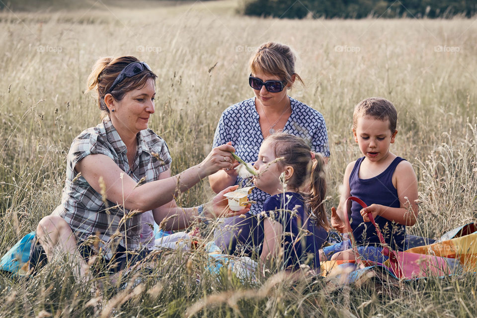 Families and friends spending time together on a meadow, close to nature. Mothers feeding kids, sitting on a blanket, on grass. Candid people, real moments, authentic situations