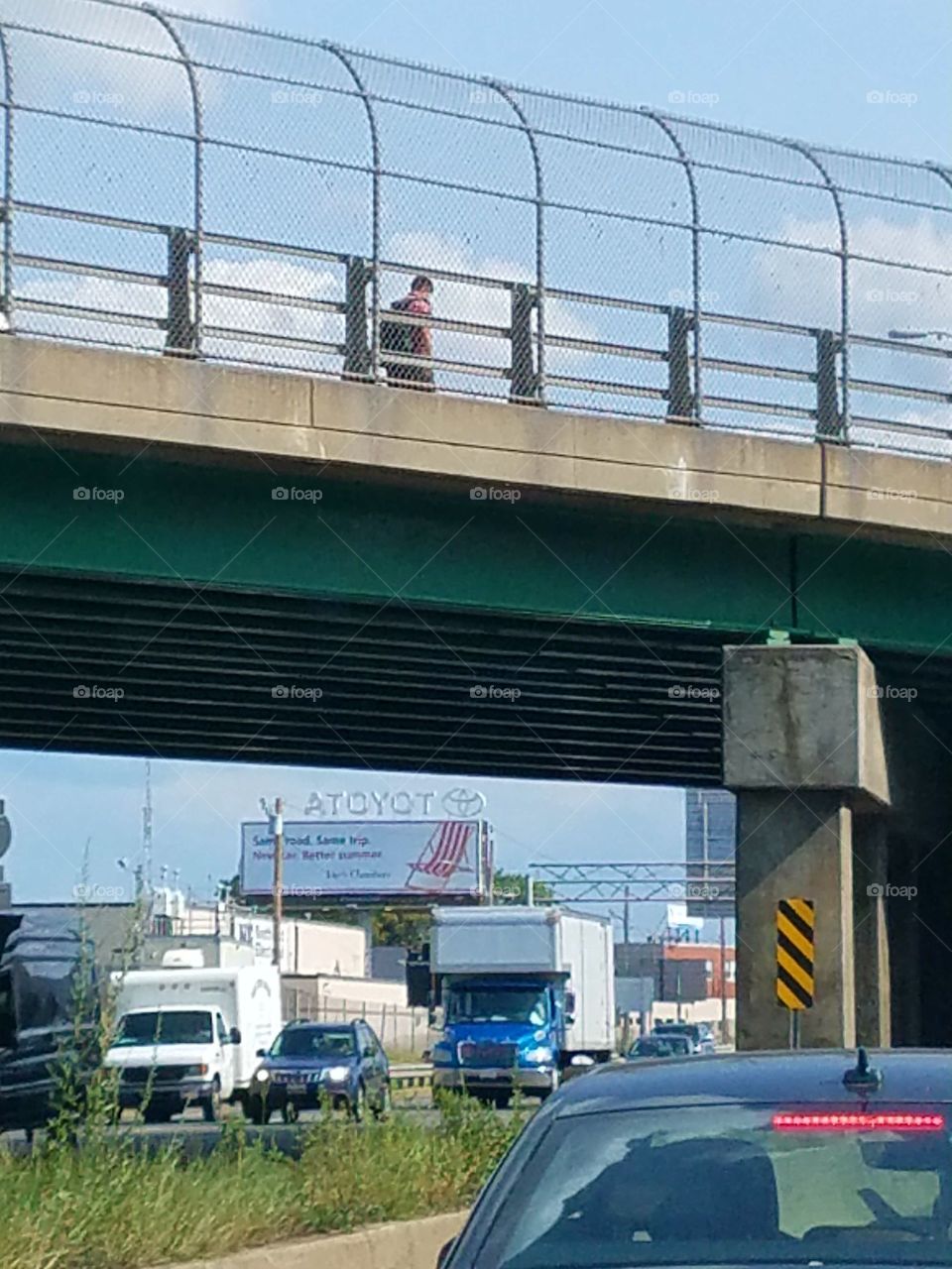 Person walking on highway overpass at rush hour.