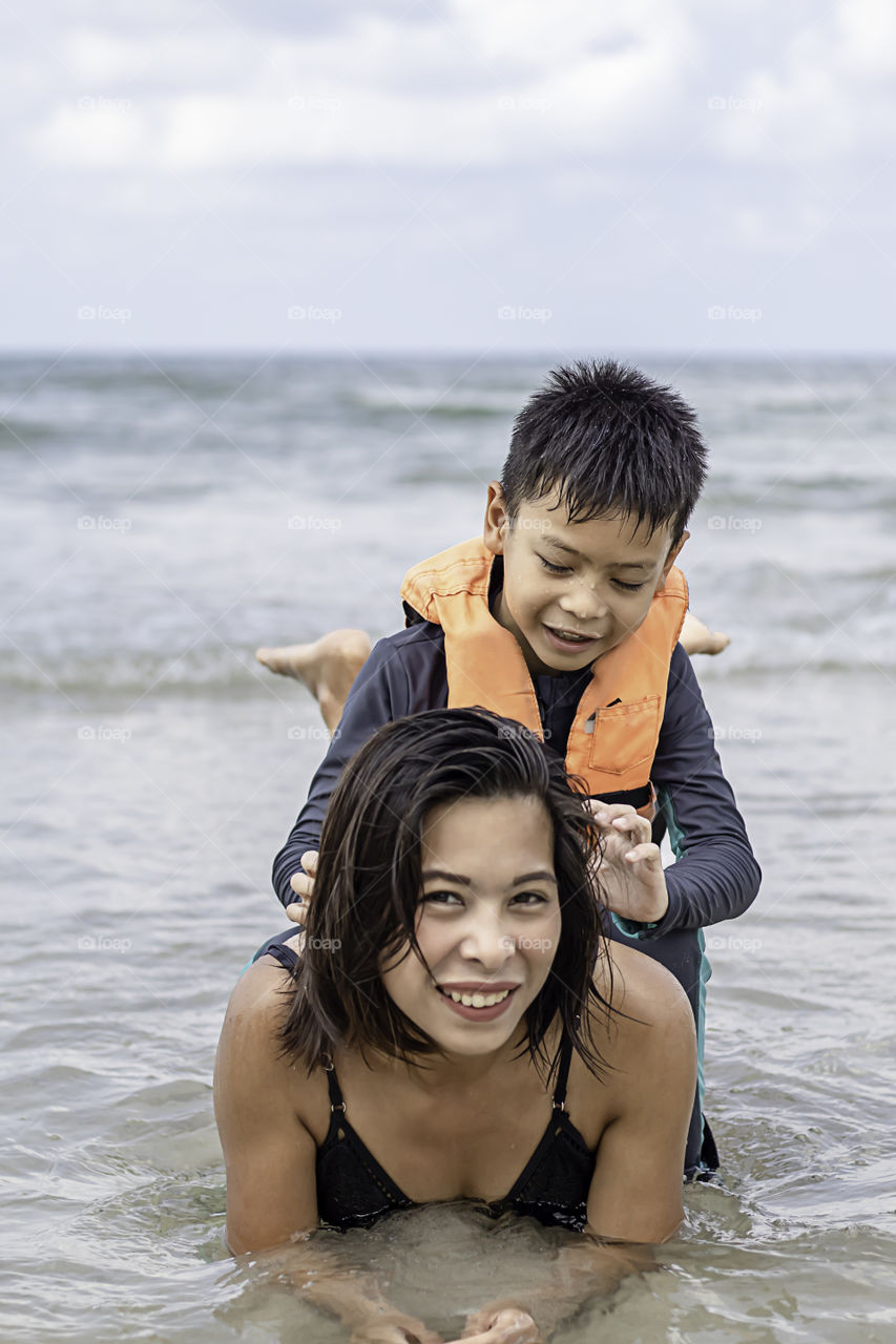 Asian boy sitting on the back of a woman playing in the sea.