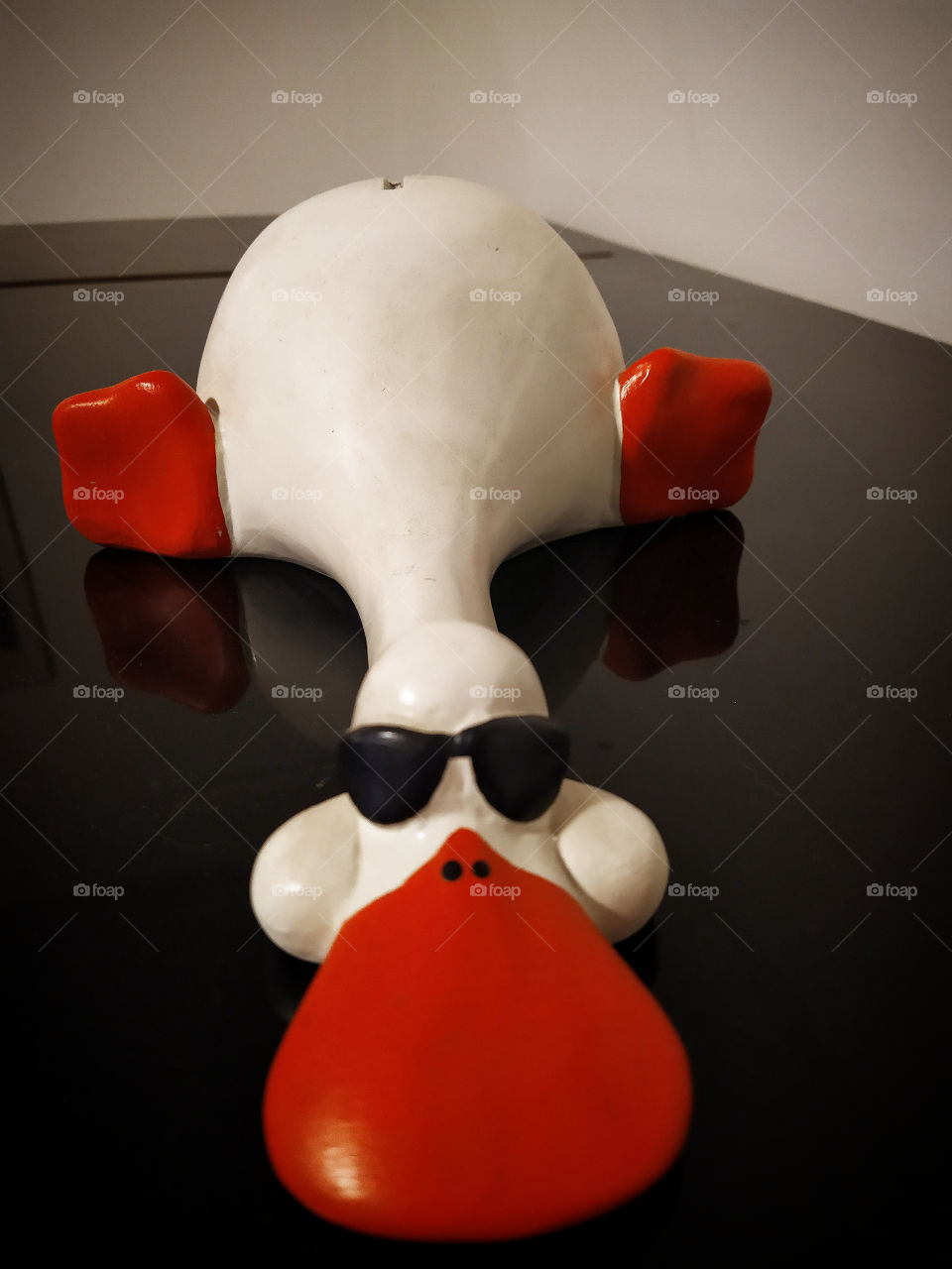 Piggy bank on a black piano.  Duck in black glasses that stretched out its head