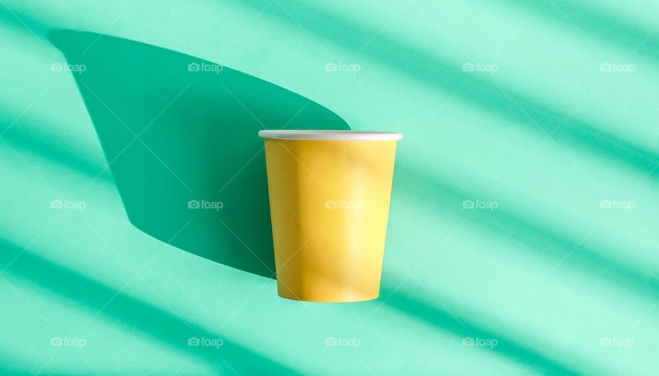 One yellow paper disposable cup is in the center on a green background with diagonal shadows, flat close-up.