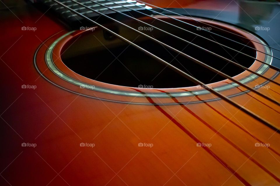 A side angle view of the body of a deeply colorful wooden acoustic guitar showing the sound hole, steel strings, and the beginning of the fret board.