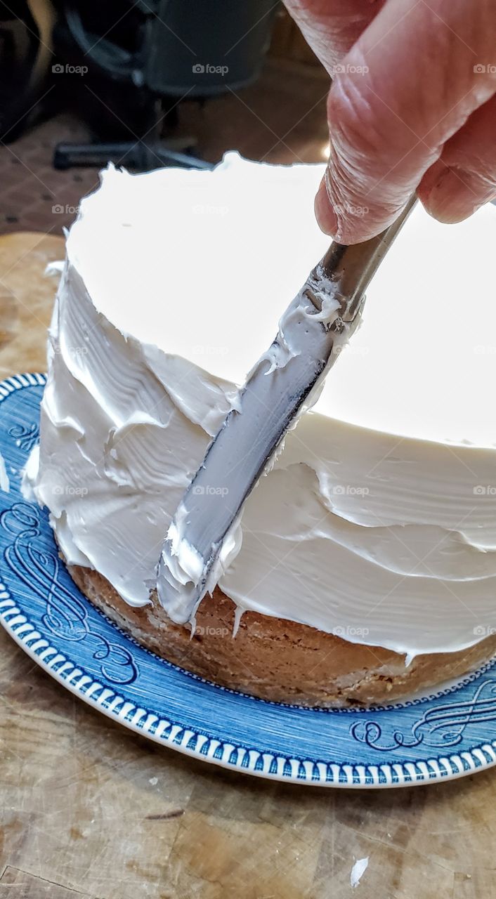 white frosting spread onto tall layer yellow cake. Decorating a home baked cake using a knife.
